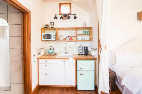 Cozy kitchen area with a retro fridge, microwave, sink, and shelves, featuring light wood and white decor.