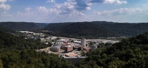 A panoramic view of a valley with buildings and hills under a partly cloudy sky.