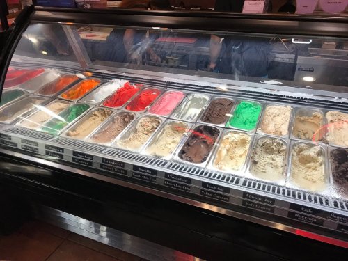 A display case filled with various colorful ice cream flavors in metal tubs.