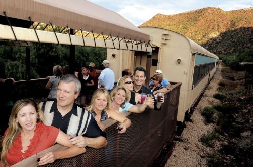 A group of people enjoying drinks on a train, with scenic mountains in the background.