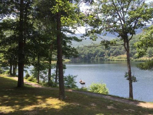 A serene lake surrounded by trees, with a small boat on the water under a clear blue sky.