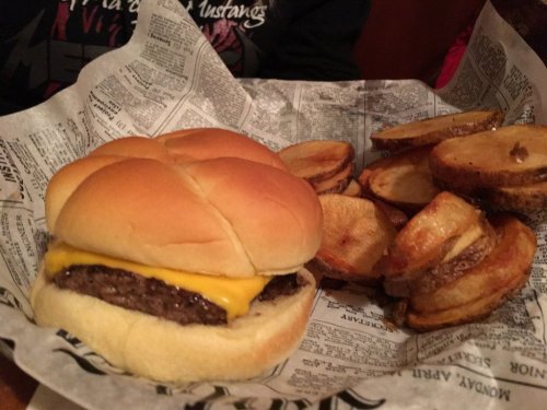 A cheeseburger with a melted slice of cheese on a bun, served with crispy potato wedges on the side.