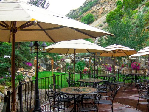 A cozy outdoor patio with tables and umbrellas, surrounded by lush greenery and colorful flowers.