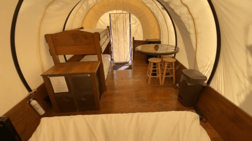 Interior of a cozy tent with bunk beds, a round table with stools, and wooden flooring.
