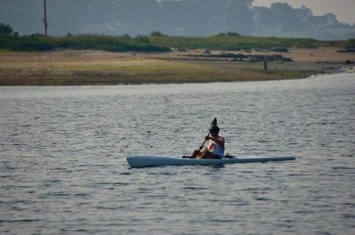 A person paddles a kayak on calm water, surrounded by a serene landscape and distant greenery.