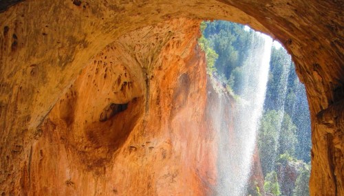 A stunning cave opening revealing a waterfall cascading into a lush green landscape.