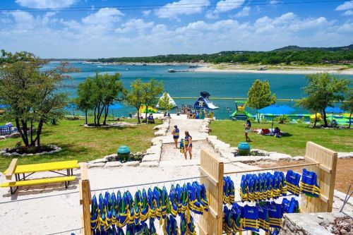 A scenic view of a lake with people enjoying water activities, surrounded by trees and colorful equipment on display.