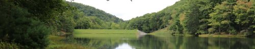 A serene lake surrounded by lush green hills and trees, reflecting the landscape in calm waters.