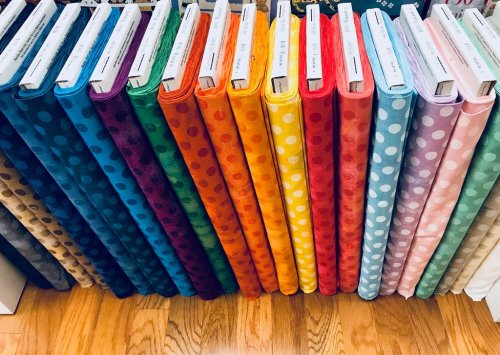 Colorful rolls of fabric in various shades, each with white polka dots, neatly arranged on a wooden surface.