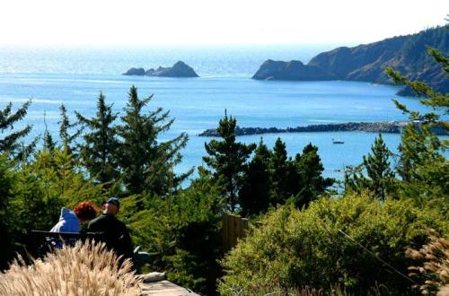 Two people sit on a bench overlooking a serene coastal view with trees and distant islands in the background.