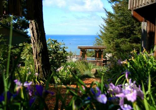A scenic view of the ocean through lush greenery and blooming flowers, with a wooden deck in the background.