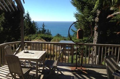 A wooden deck with a table and chairs overlooks a serene ocean view surrounded by trees.