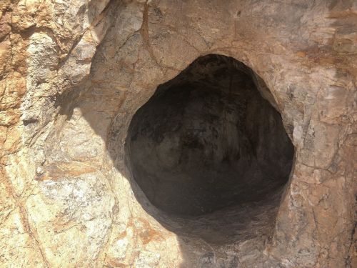 A circular cave entrance in a rocky surface, revealing a dark interior.