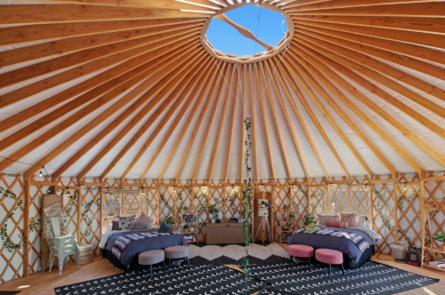 Interior of a yurt featuring two beds, a circular skylight, and wooden beams, creating a cozy, rustic atmosphere.