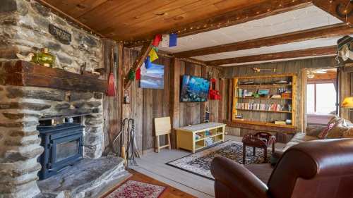 Cozy living room with a stone fireplace, wooden walls, bookshelves, and colorful decor, featuring a TV and comfortable seating.