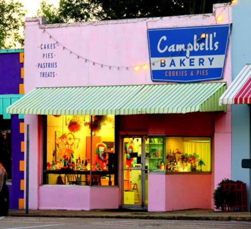 A colorful bakery storefront with a striped awning, featuring a sign for "Campbell's Bakery" and bright window displays.