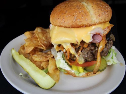 A large cheeseburger with lettuce, tomato, pickles, and crispy onions, served with potato chips and a pickle slice.
