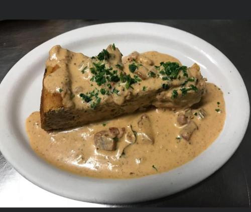 A slice of bread topped with creamy sauce and herbs, served on a white plate with a rich, savory gravy.