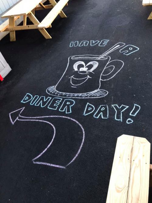 Chalk drawing on pavement featuring a smiling coffee cup and the text "Have a Diner Day!" with an arrow.