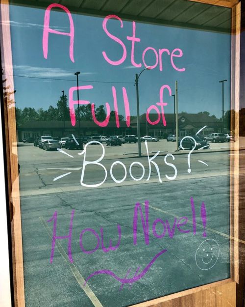 A store window displays a playful sign: "A Store Full of Books? How Novel!" in colorful lettering.
