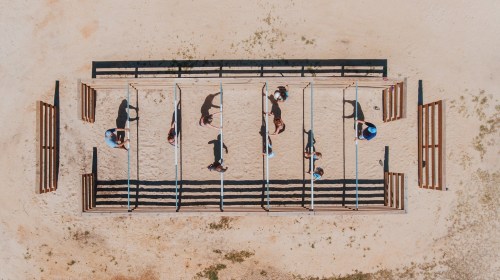Aerial view of people navigating an obstacle course with horizontal bars on a sandy ground.