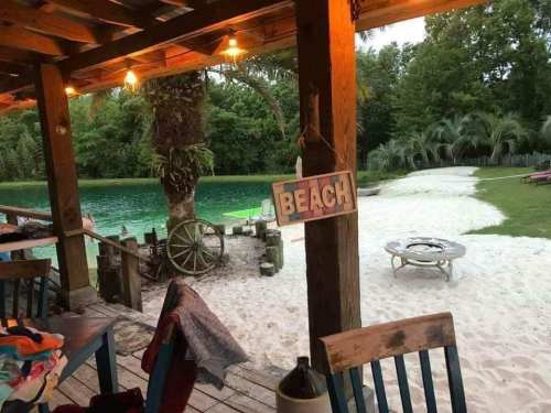A cozy beachside scene with a wooden deck, a "BEACH" sign, and a view of a sandy area and green water.