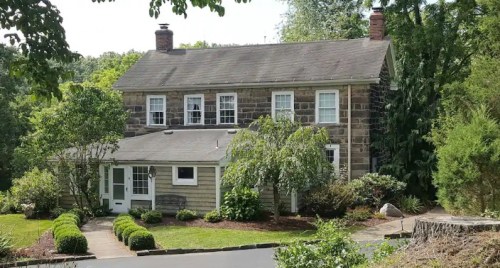 A two-story stone and wood house surrounded by greenery and a well-maintained garden.