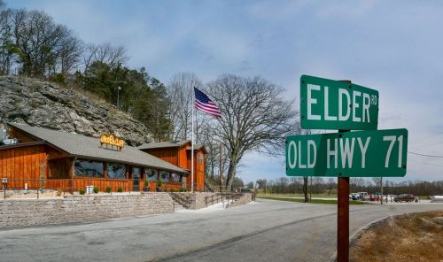 A wooden building with an American flag, next to a street sign for Elder Rd and Old Hwy 71.