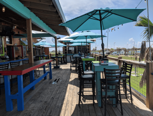 Outdoor dining area with colorful tables and umbrellas, overlooking a sunny waterfront.