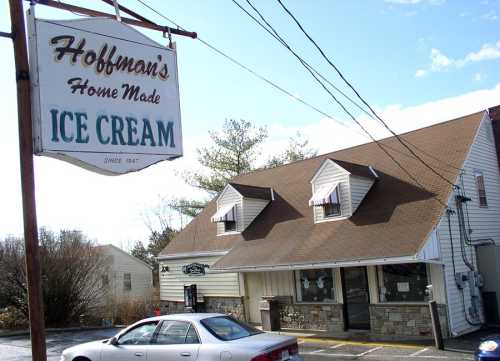 A quaint ice cream shop with a sign reading "Hoffman's Home Made Ice Cream," featuring a stone facade and a car parked outside.