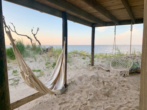 A serene beach scene featuring two hammocks under a wooden structure, with sand and ocean in the background.