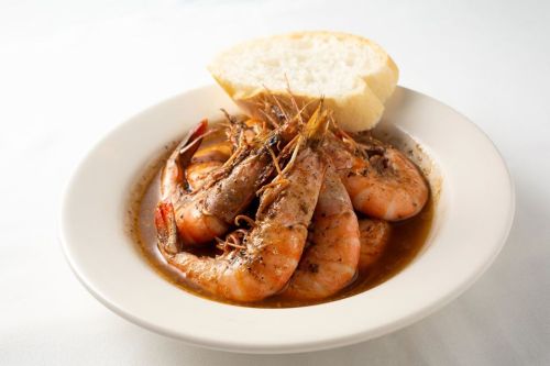 A bowl of shrimp in a savory sauce, served with a slice of bread on the side.