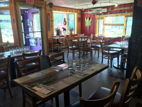 Interior of a restaurant with wooden tables, chairs, and colorful decor, set for dining with glasses and utensils.