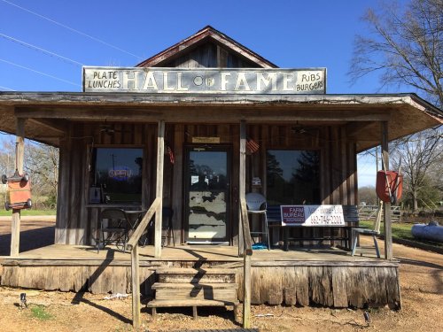 A rustic restaurant named "Hall of Fame" with a porch, offering ribs and burgers, set in a rural area.