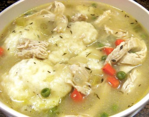 A bowl of chicken and dumpling soup with shredded chicken, vegetables, and fluffy dumplings in a savory broth.
