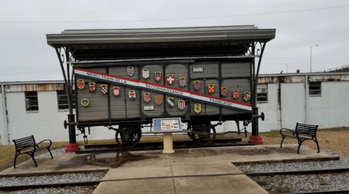 A historic train car display featuring various shields, with benches nearby and a building in the background.