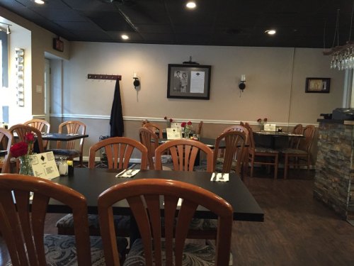 A cozy restaurant interior with wooden chairs, tables set for dining, and decorative elements on the walls.