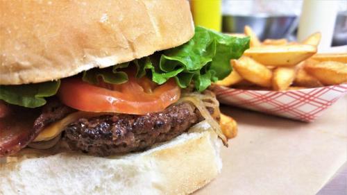 A close-up of a juicy hamburger with lettuce, tomato, and bacon, served with a side of golden fries.