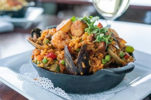 A vibrant seafood paella with shrimp, mussels, and vegetables served in a black dish, garnished with herbs.