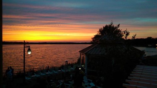 A serene sunset over a lake, with vibrant orange and purple hues reflecting on the water and silhouettes of trees.