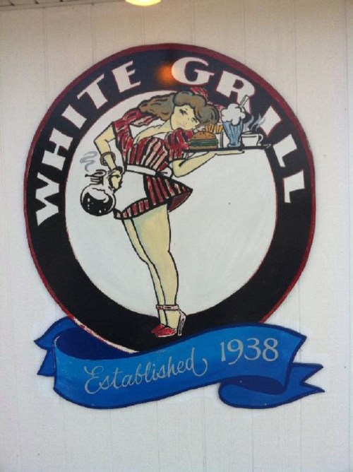 A vintage sign for "White Grill," featuring a woman in a striped outfit holding a drink, established in 1938.
