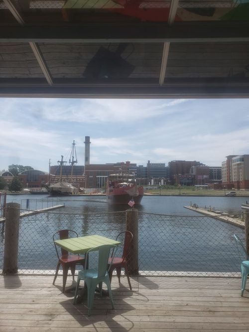 View of a harbor with a ship, buildings in the background, and a table with chairs in the foreground.