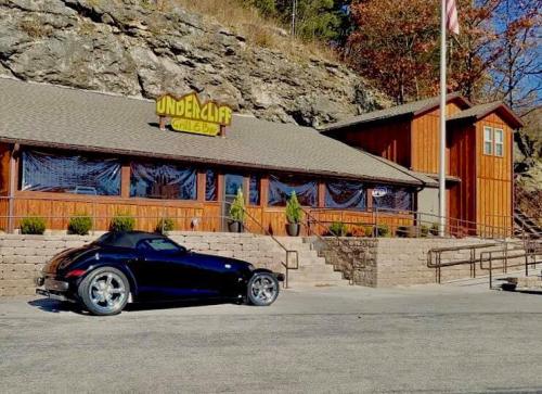 A sleek black convertible parked in front of a rustic wooden restaurant with large windows and an American flag.