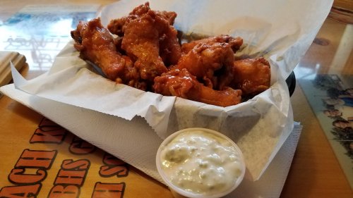 A plate of crispy chicken wings with a side of creamy dipping sauce, served on a paper-lined tray.