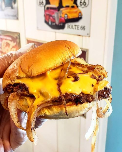 A hand holding a cheeseburger with melted cheese and grilled onions on a soft bun, set against a retro diner backdrop.