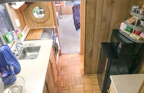 A cozy kitchen area with wooden cabinets, a sink, and a view of a hallway leading to a bedroom.