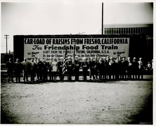A historic black-and-white photo of a group of people in front of a large banner about a raisin donation for a food train.
