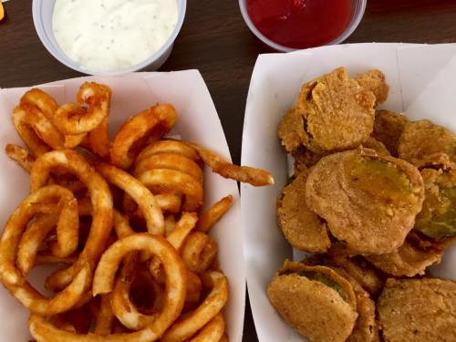A plate of curly fries and fried pickles, served with dipping sauces.