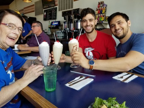A group of three people, including an older woman and two young men, enjoy milkshakes at a diner.