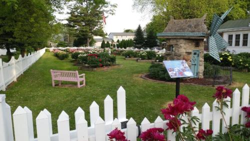 A picturesque garden with a stone structure, colorful flowers, a pink bench, and a white picket fence.